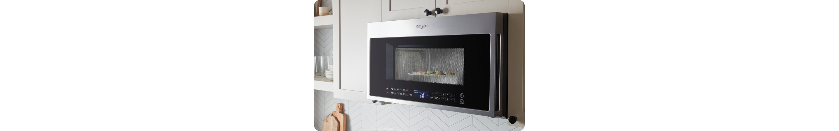 Un four à micro-ondes Whirlpool dans lequel cuisent des aliments. À proximité se trouvent des planches à découper et des étagères contenant des objets comme des verres