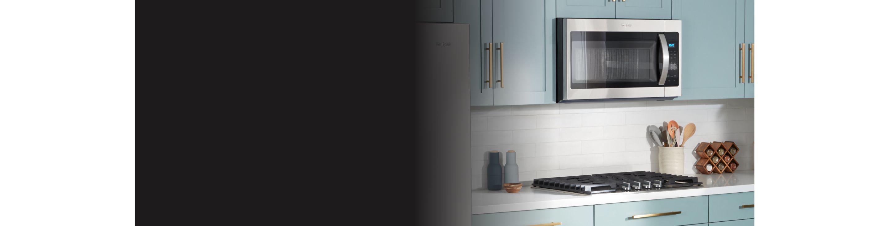 Un four à micro-ondes Whirlpool au-dessus d'une table de cuisson. Les appareils de cuisine sont entourés d'une étagère à épices, d'un porte-ustensiles, d'une salière et poivrière et d'un petit bol en bois