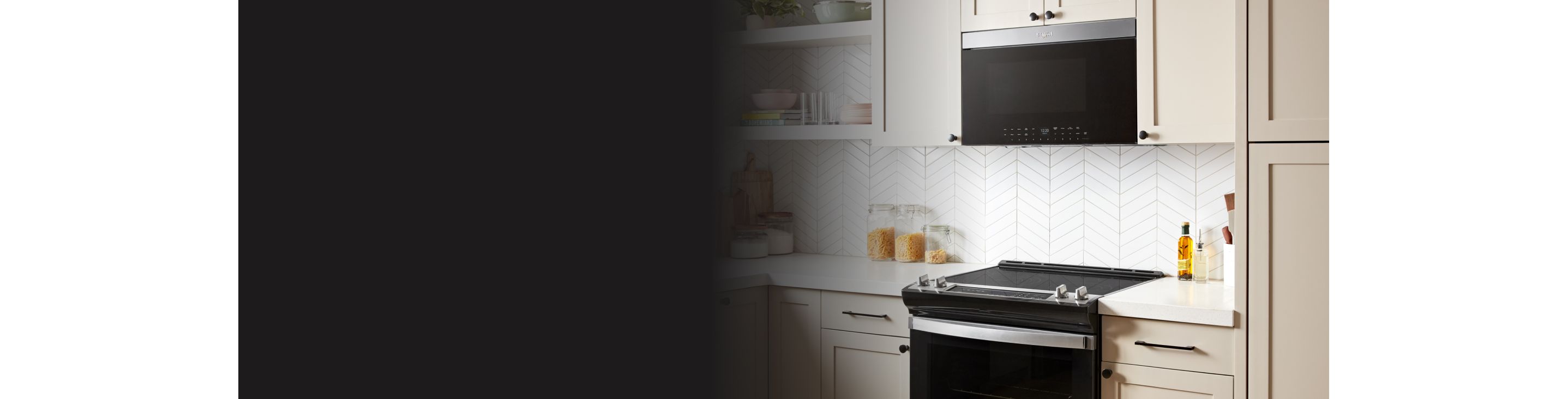 Une cuisine blanche avec un four à micro-ondes encastré Whirlpool au-dessus d'une cuisinière à induction Whirlpool. Sur les comptoirs, on voit des bocaux en verre contenant des pâtes et de la farine, des récipients d'huile et des planches à découper. Sur les étagères du haut, on voit des livres de cuisine, des verres et des bols