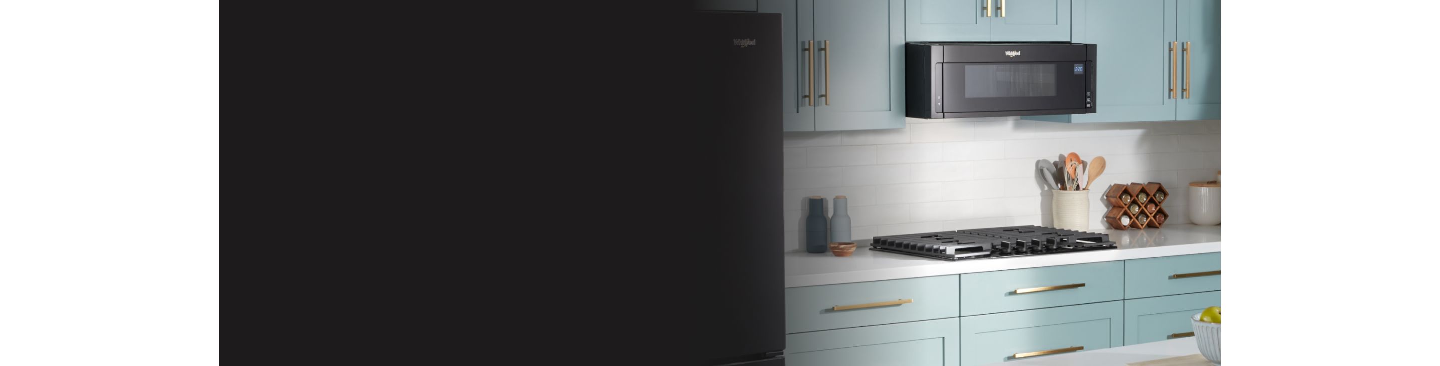 Une cuisine avec des armoires vertes est équipée d'un four à micro-ondes Whirlpool au-dessus d'une table de cuisson Whirlpool. Sur les comptoirs se trouvent une salière et une poivrière, un porte-ustensiles, une étagère à épices, un petit bol en bois et un récipient