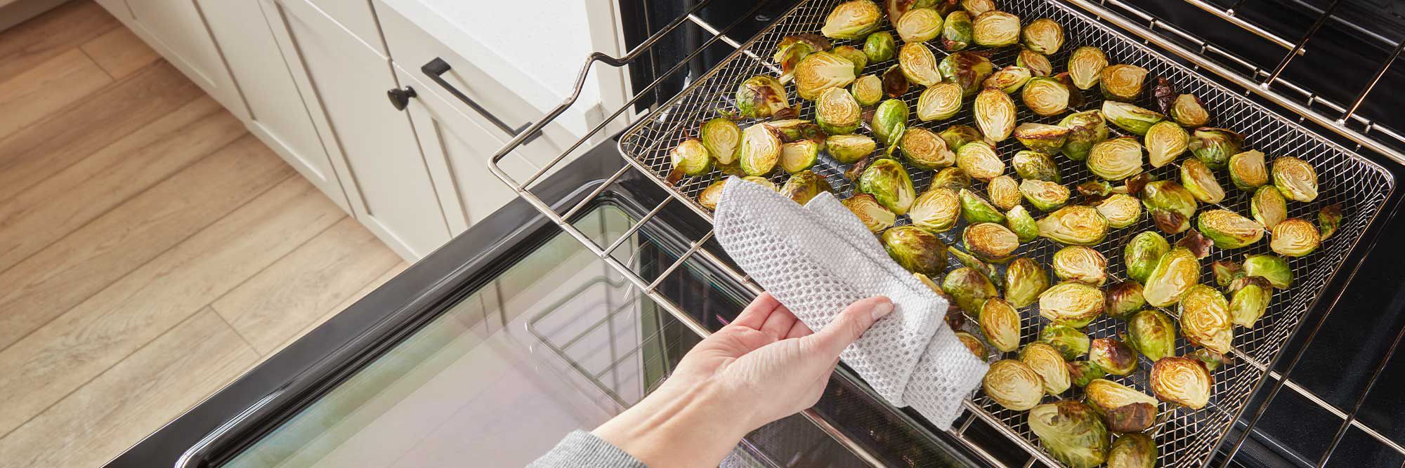 Une personne sort un panier à friture rempli de choux de Bruxelles rôtis d'un four Whirlpool à l'aide d'un chiffon à vaisselle