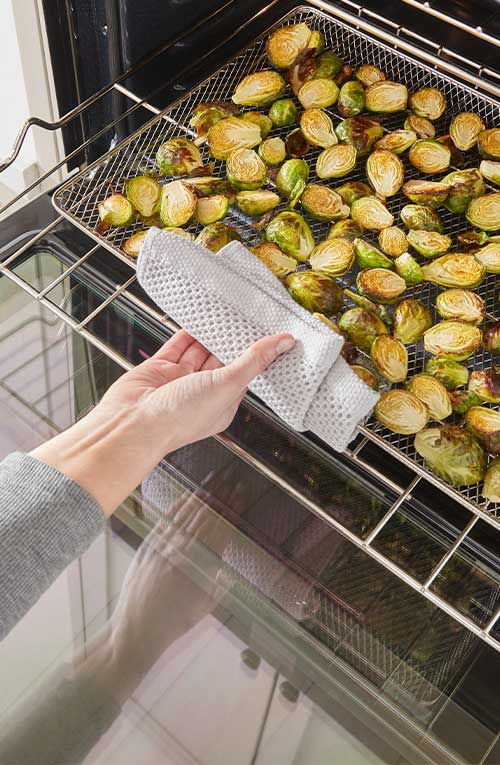 Une personne sort un panier à friture rempli de choux de Bruxelles rôtis d'un four Whirlpool à l'aide d'un chiffon à vaisselle