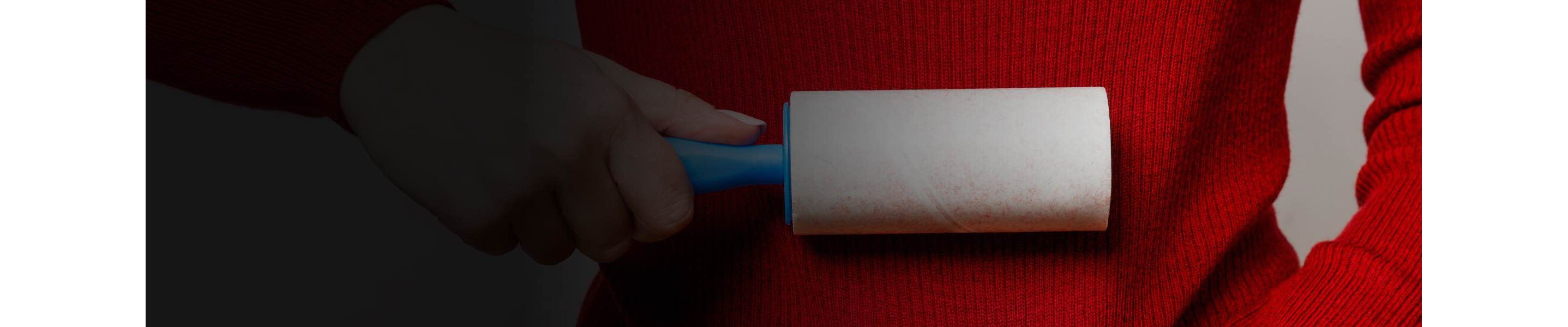 A person holds a lint roller up against a red sweater