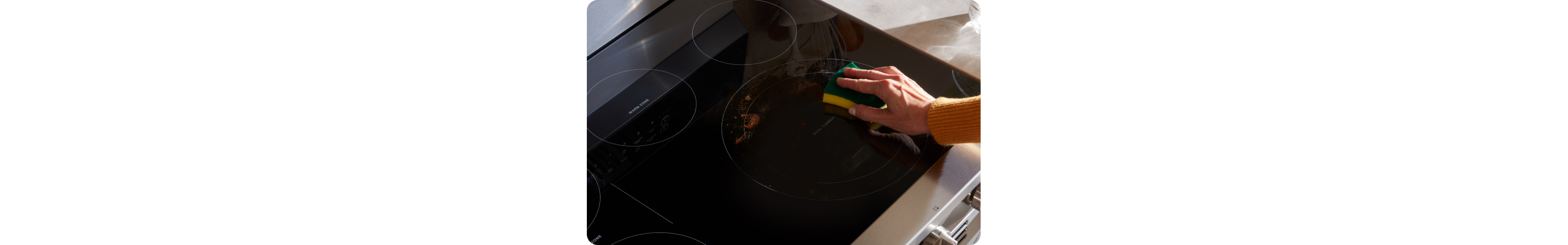 Someone scrubs the cooktop of a Whirlpool Oven with a sponge