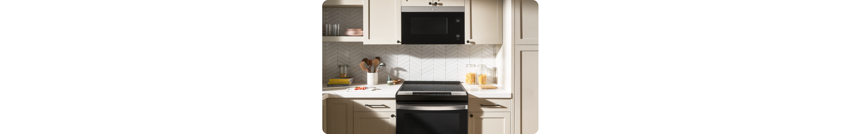 A kitchen with a Whirlpool Range and over-the-range microwave. On the counters are a full utensil holder, containers of pasta, cookbooks and other various items