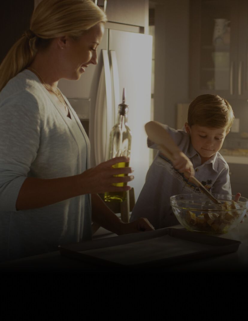 Mom and son using a tablet, mixing bowl and sheet pan on the countertop to make a recipe together.