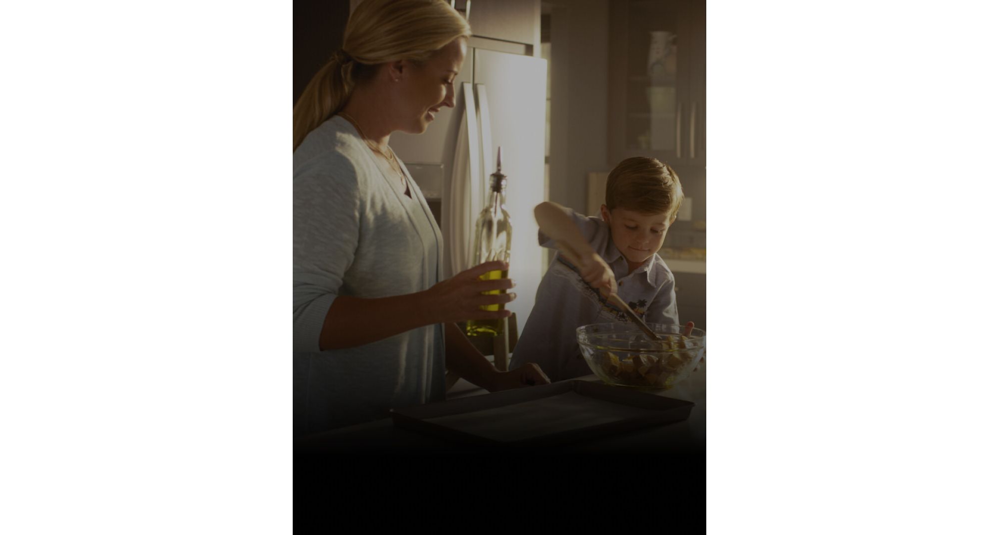 Mom and son using a tablet, mixing bowl and sheet pan on the countertop to make a recipe together.