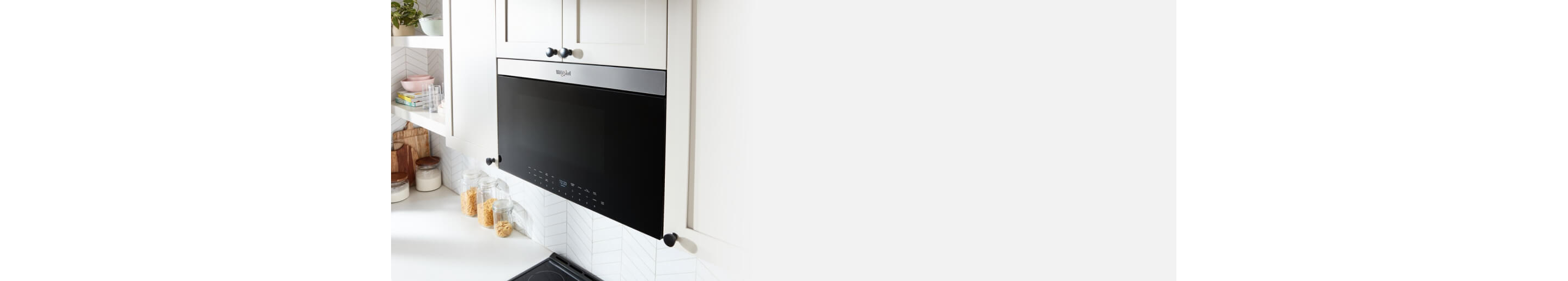 A flush Maytag Over-the-Range Microwave above a Maytag Cooktop surrounded by white cabinets. On the counters are jars of pasta and flour and cutting boards