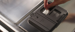 A hand placing a dishwasher detergent pod into a dispenser